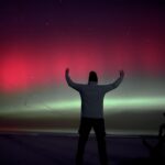 Spektakularna zorza polarna nad morzem w Dębkach – sylwetka osoby na tle kolorowego nieba