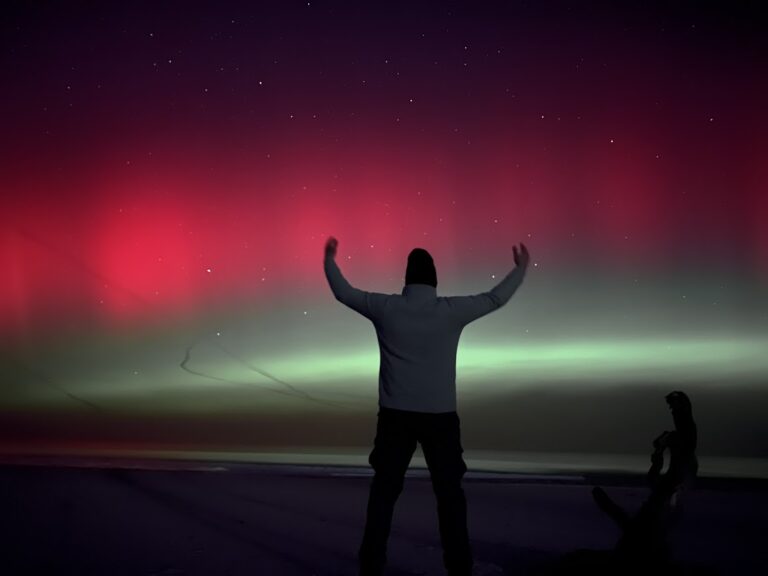 Spektakularna zorza polarna nad morzem w Dębkach – sylwetka osoby na tle kolorowego nieba