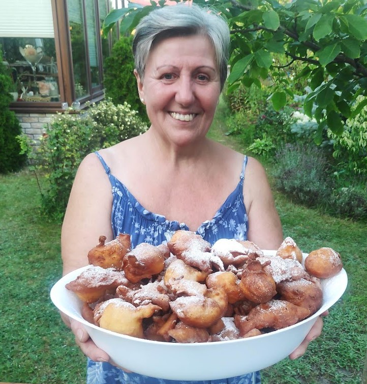 Pani Danusia, gospodyni Villa NOVA Dębki, trzyma półmisek domowych pączków w ogrodzie