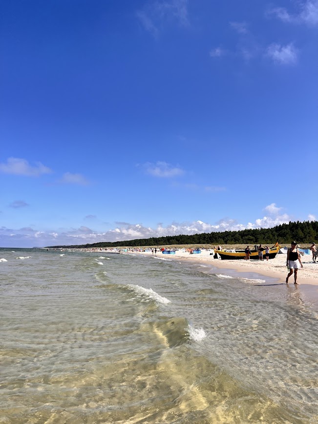 Szeroka plaża w Dębkach z krystalicznie czystą wodą Bałtyku, jasnym piaskiem i łodzią rybacką w oddali pod błękitnym niebem