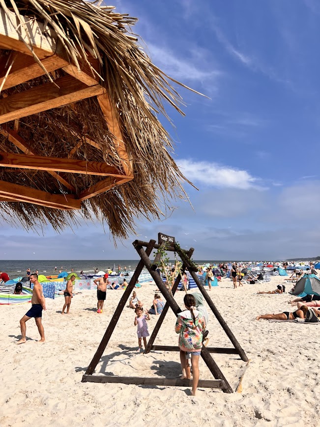 Drewniana huśtawka i parasole kryte strzechą na szerokiej plaży w Dębkach, biały piasek i wakacyjny klimat