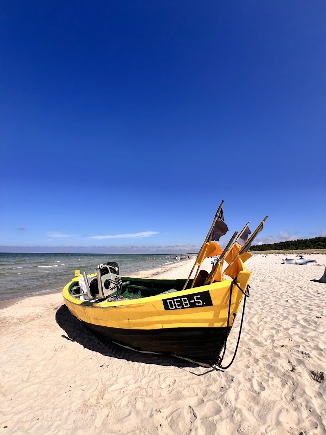 Żółta łódź rybacka z oznaczeniem DEB-S na szerokiej plaży w Dębkach, błękitne niebo i jasny piasek