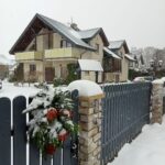 Villa NOVA w Dębekach zimą – zaśnieżony budynek pensjonatu z dekoracyjnym wieńcem na płocie