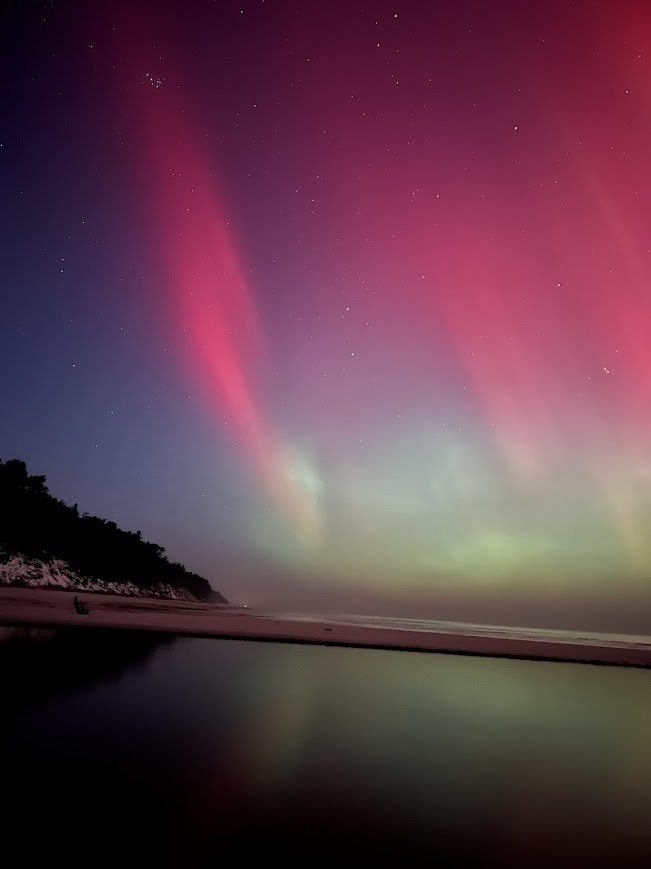 Spektakularna, pionowa fotografia różowej i zielonej zorzy polarnej nad wodą w Dębkach poza sezonem, z widocznym odbiciem świateł w tafli