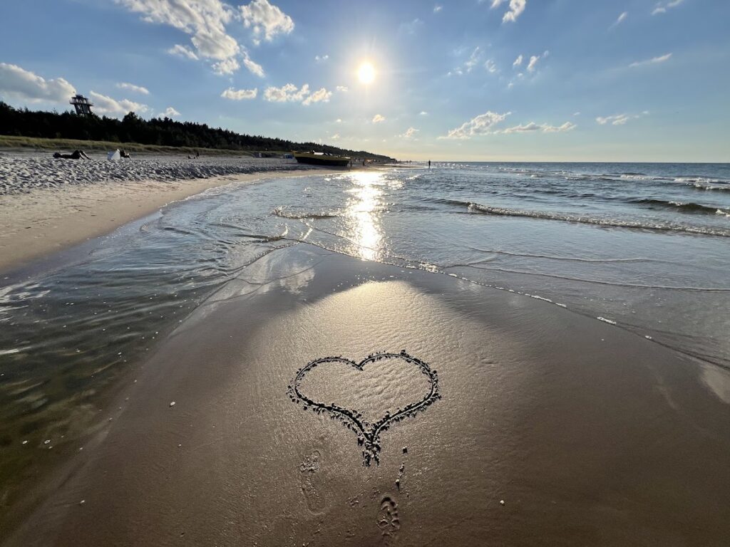 Romantyczny symbol serca narysowany na mokrym piasku plaży w Dębkach z widokiem na morze i słońce w tle