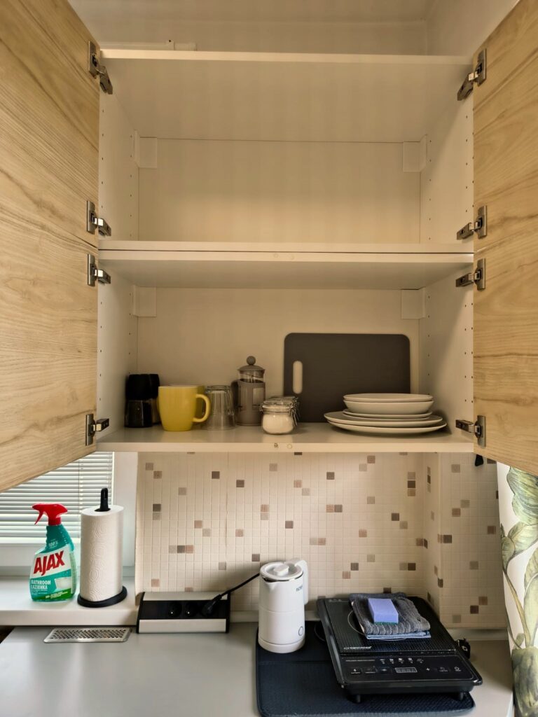 Otwarta szafka kuchenna z naczyniami, kubkami i akcesoriami w aneksie kuchennym apartamentu w Villa NOVA w Dębkach