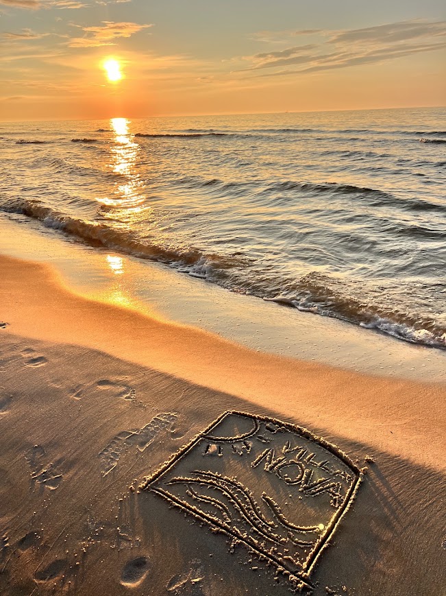 Logo Villa NOVA wyryte na piasku podczas zachodu słońca na plaży w Dębkach