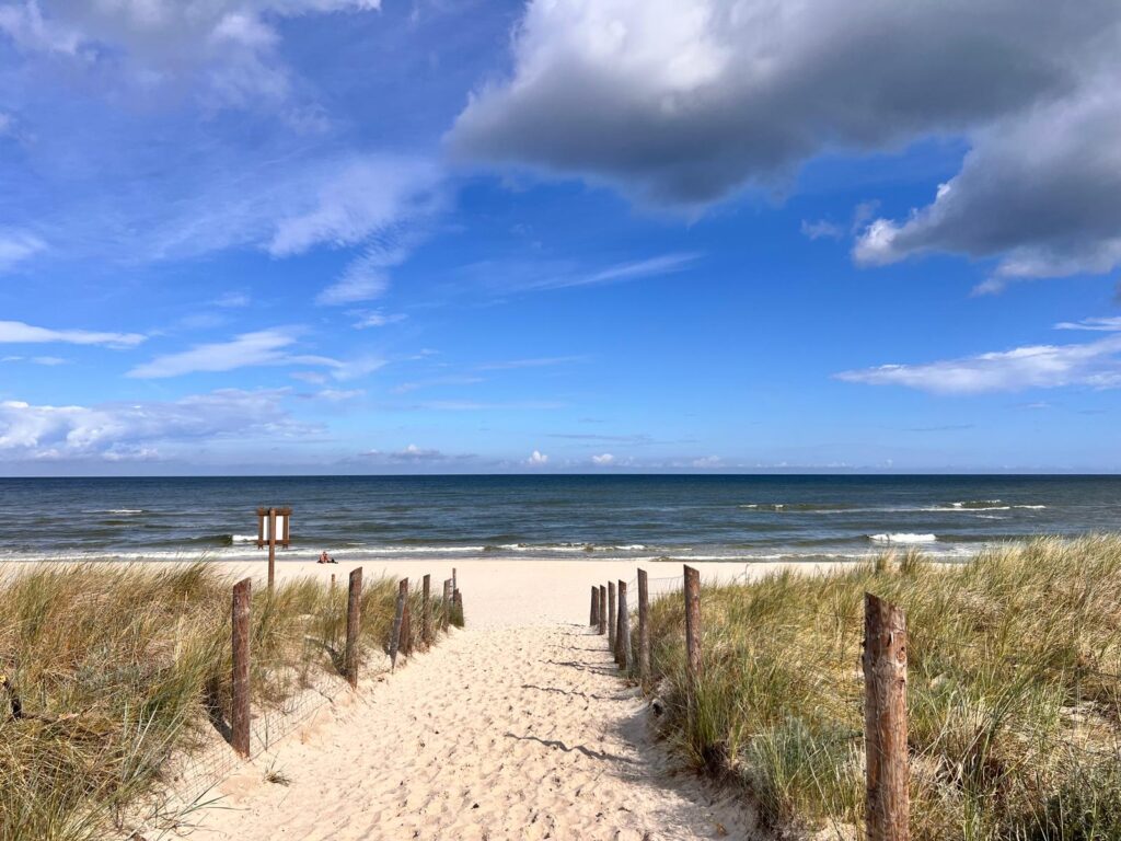 Malownicze, piaszczyste wejście na plażę przez wydmy w Dębkach we wrześniu z widokiem na morze i błękitne niebo