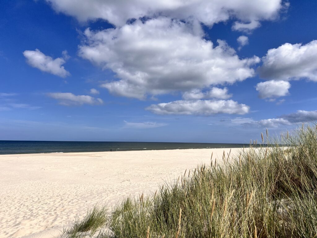 Szeroka piaszczysta plaża i nadmorskie wydmy w Dębkach pod błękitnym niebem z chmurami