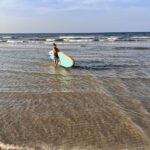 Osoba wchodząca z deską SUP w fale Morza Bałtyckiego na plaży w Dębkach