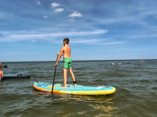 Chłopiec pływający na desce SUP w morzu na plaży w Dębkach