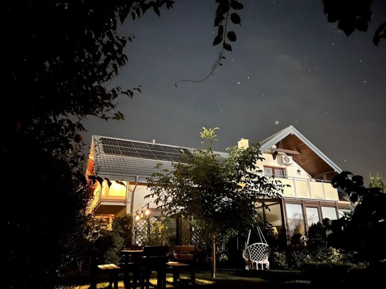 Oświetlona nocą Villa NOVA w Dębkach pod rozgwieżdżonym niebem, z widocznym ogrodem i pergolą