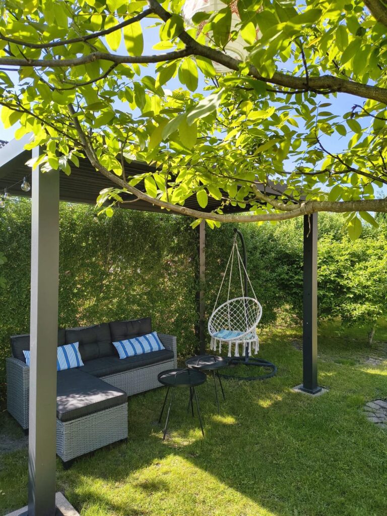 Nowoczesna pergola w zielonym ogrodzie Villi NOVA w Dębkach z wygodną sofą i wiszącym fotelem